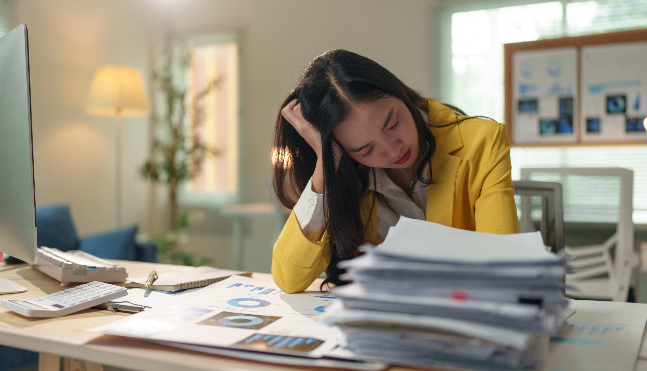 Frustrated employee at a desk surrounded by overflowing inbox notifications or sticky notes, tired or overwhelmed expression, dim or cluttered modern office, conveys hidden stress and lost productivity.